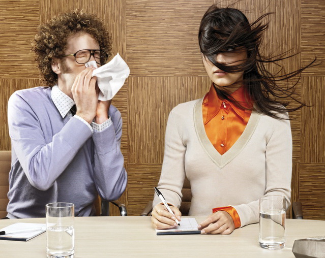 Man sneezing on woman in office environment