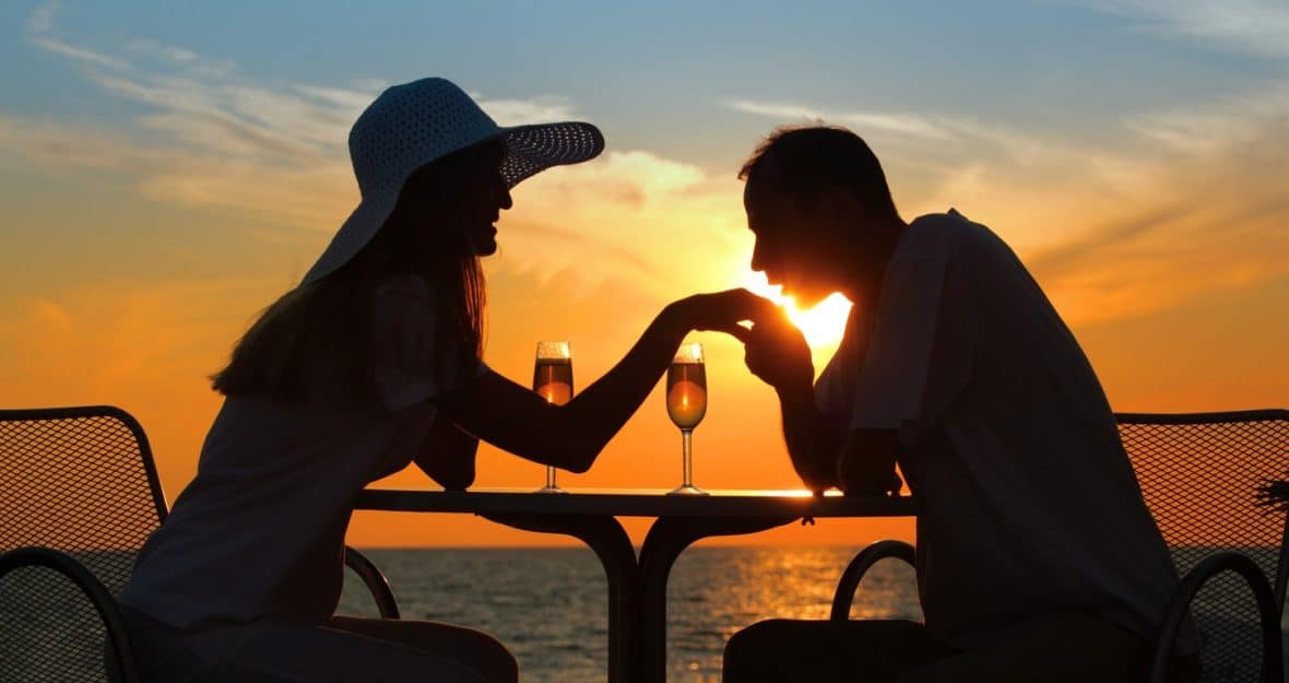 man kisses  hand to  woman on sunset behind  table outside
