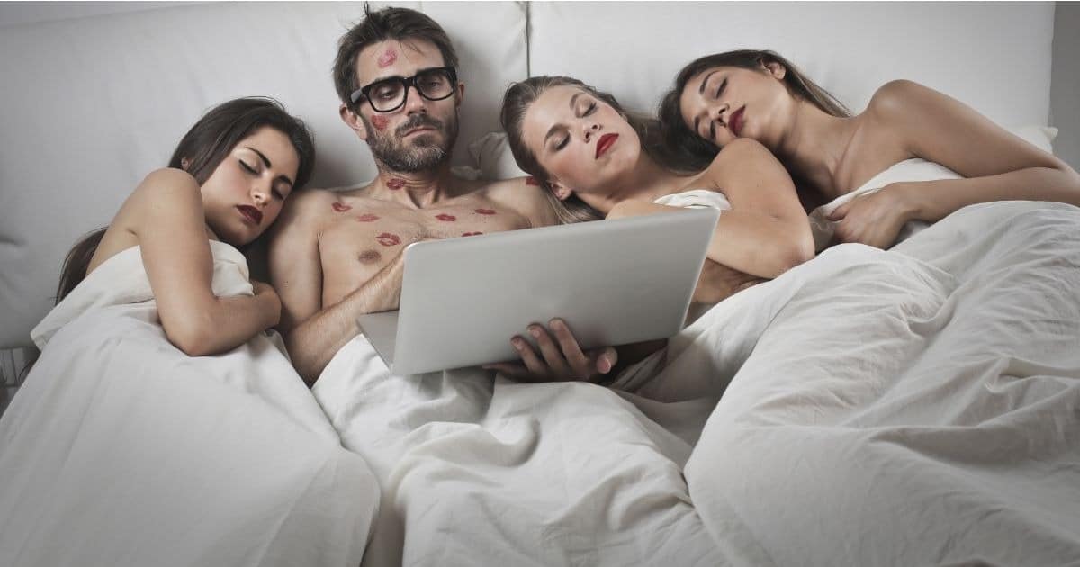 парень лежит в постели с 3 девушками
