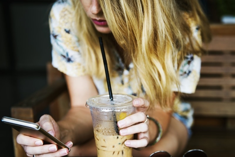 Девушка смотрит в смартфон и пьет коктейль