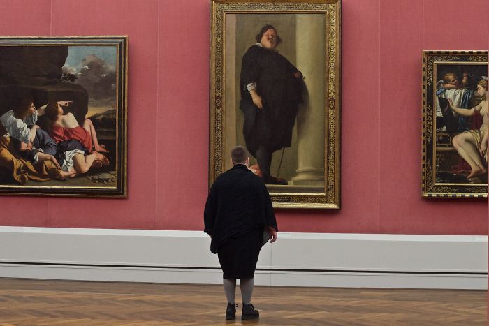 полная женщина смотрит на картину полного человека в музее