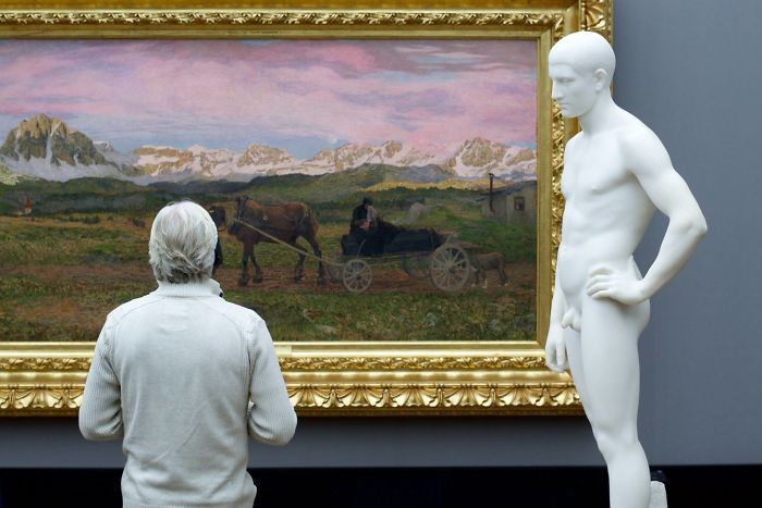 мужчина в белом свитере смотрит в музее на картину