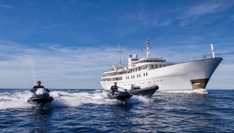 водные мотоциклы и лодка сопровождают движение яхты в открытом море.