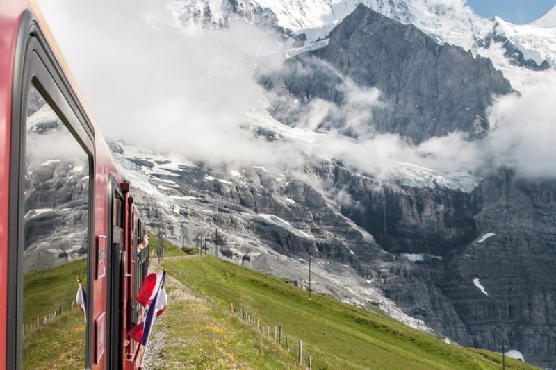 поезд с красными вагонами идет по равнине на фоне высоких гор