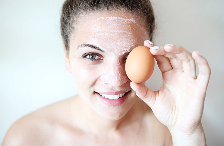 Девушка в маске держит яйцо возле глаза