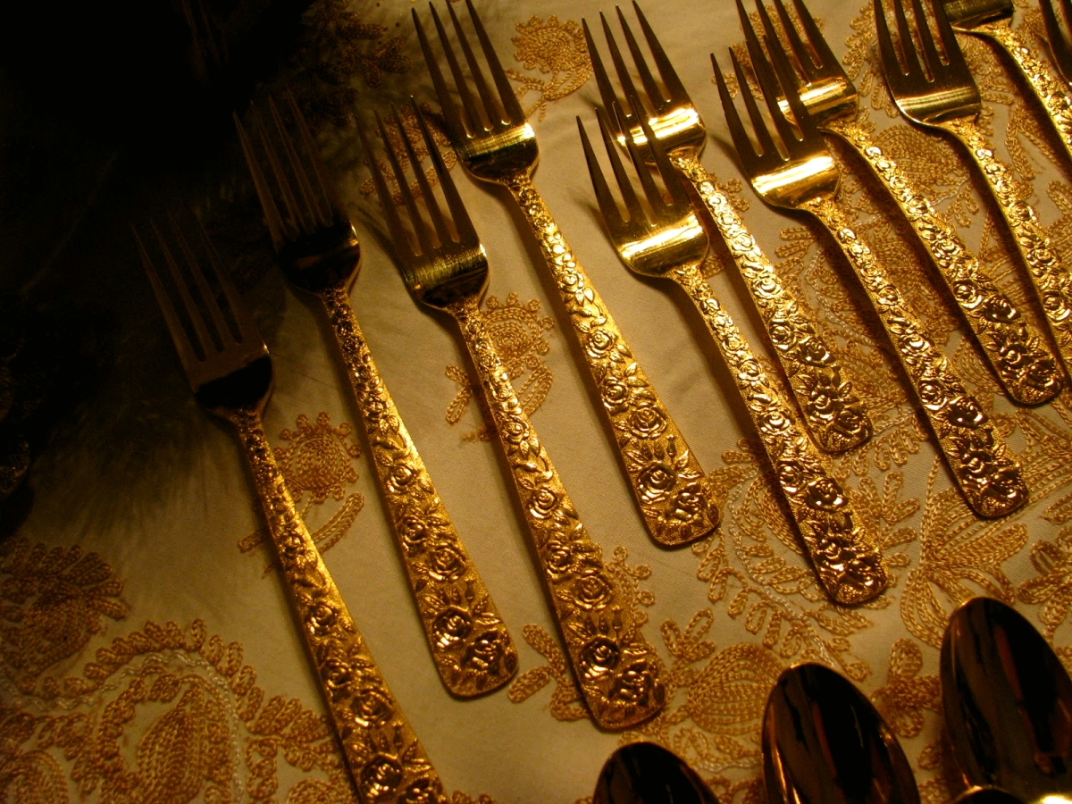 сложенные в ряд на столе золотые вилки и ложки