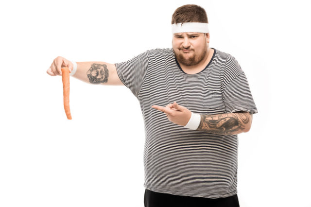 полный мужчина держит морковь в руке