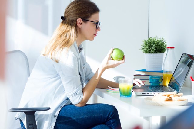 девушка с яблоком сидит перед ноутбуком
