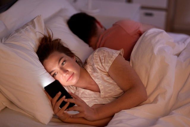 девушка с телефоном рядом со спящим мужчиной