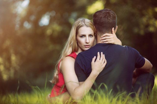 девушка обнимает парня, сидя в траве