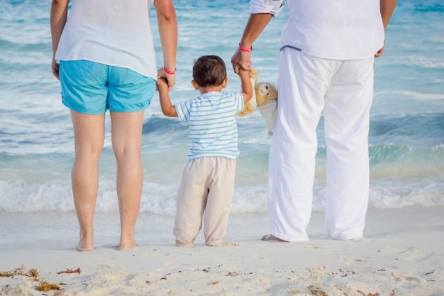 папа и мама держат за руки сына на берегу моря