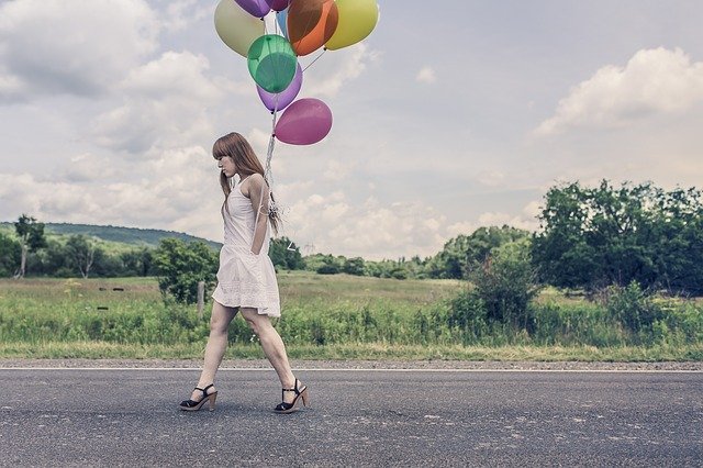 девушка с воздушными шарами идет по дороге