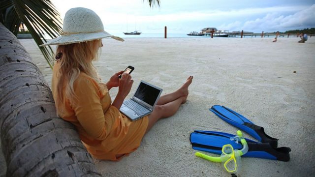 девушка на пляже с телефоном и ноутбуком