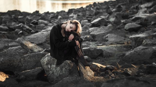 девушка сидит на берегу в черном платье