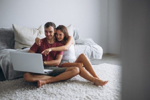 парень и девушка смотрят ноутбук, сидя на полу у кровати