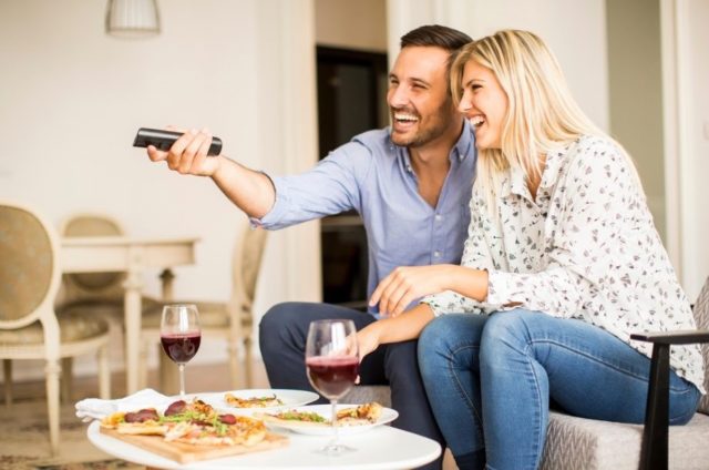 пара пьет вино и смотрит телевизор дома