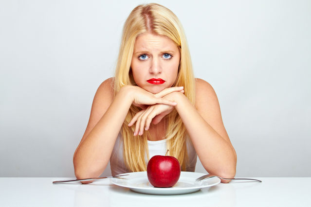 блондинка сидит перед тарелкой с красным яблоком