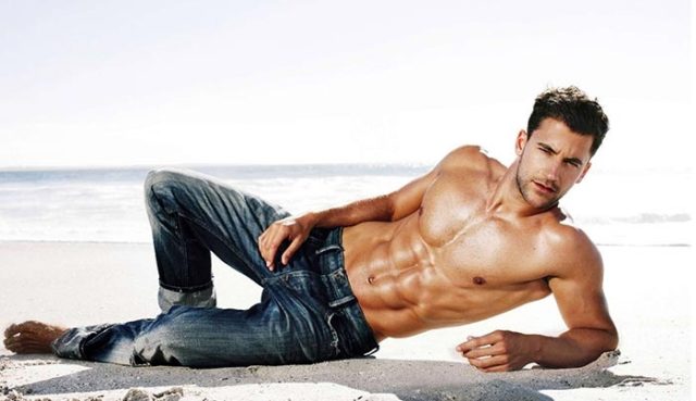 мускулистый парень в джинсах лежит на пляже