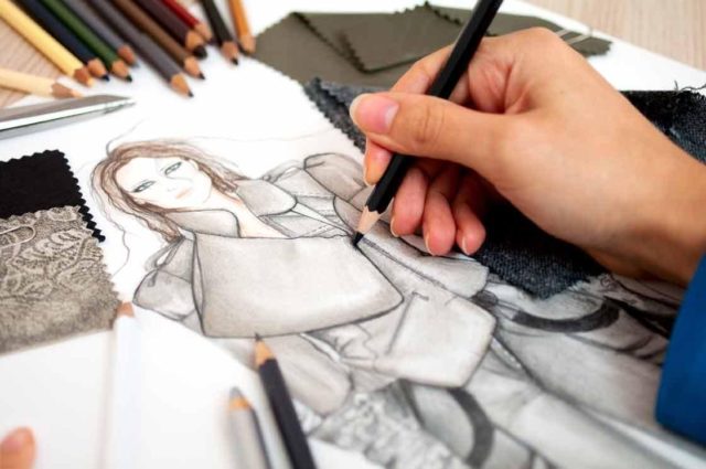 девушка рисует черным карандашом плащ