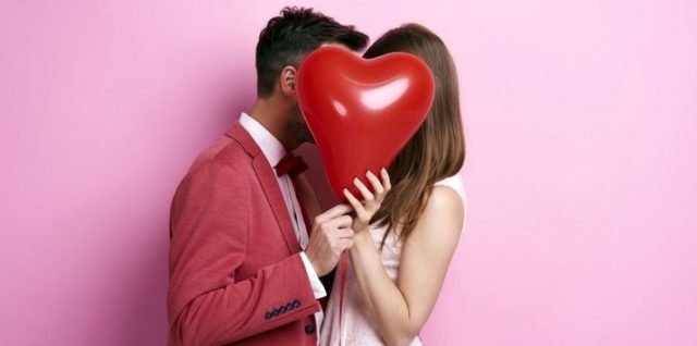 молодая пара целуется, прикрывшись шаром в форме сердца