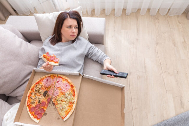 девушка лежит с коробкой пиццы на диване