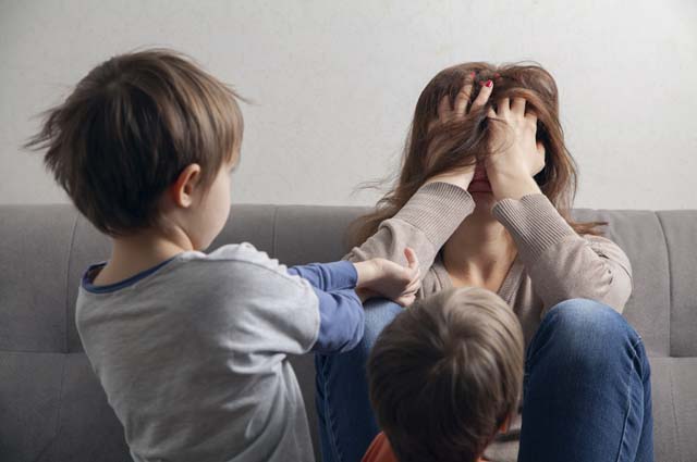 женщина закрыла руками лицо рядом с детьми